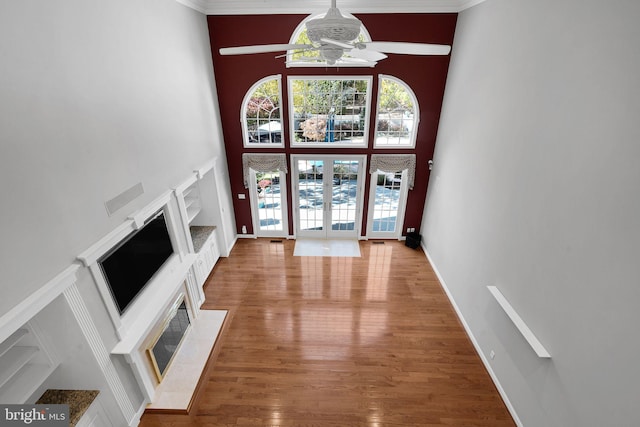 unfurnished living room featuring wood-type flooring, french doors, ornamental molding, a high ceiling, and ceiling fan