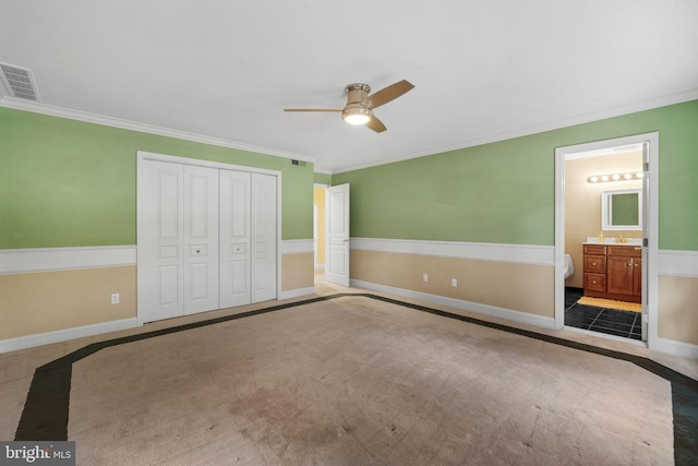 unfurnished bedroom with a closet, carpet floors, connected bathroom, crown molding, and ceiling fan