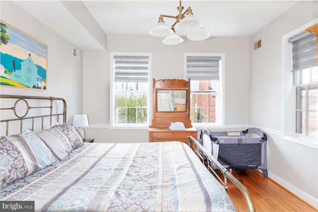 bedroom with multiple windows, wood-type flooring, and a chandelier