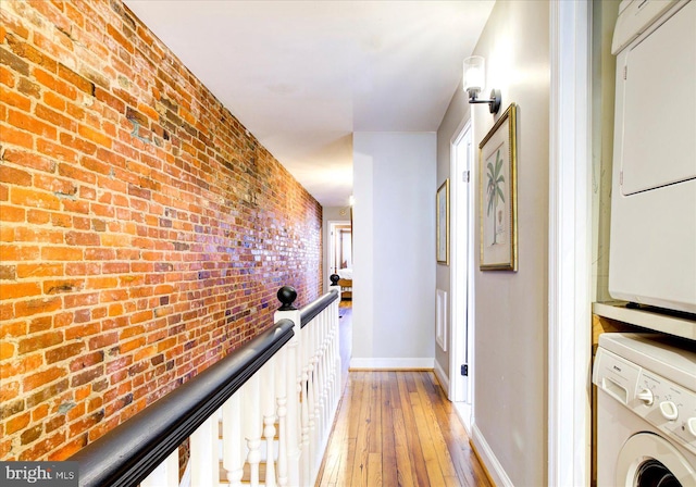 corridor with light hardwood / wood-style flooring, brick wall, and stacked washer and clothes dryer