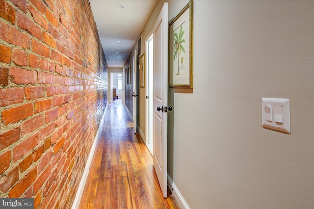 hallway featuring hardwood / wood-style flooring and brick wall