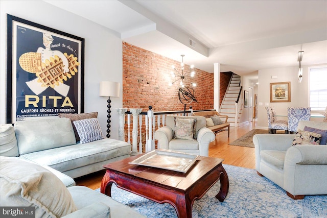 living room with wood-type flooring, a chandelier, and brick wall