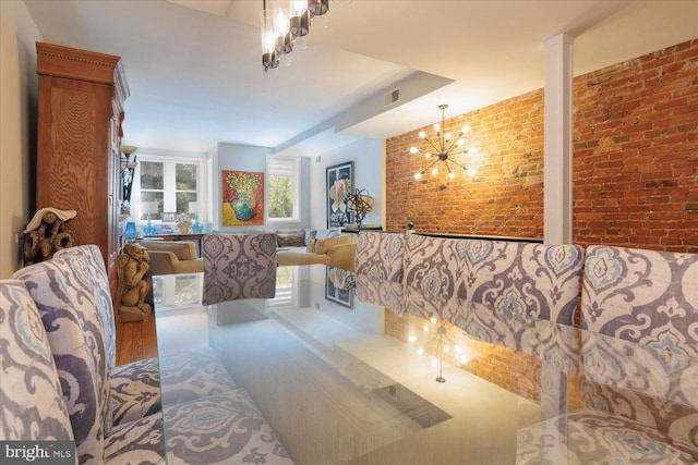 living room with brick wall, an inviting chandelier, and decorative columns