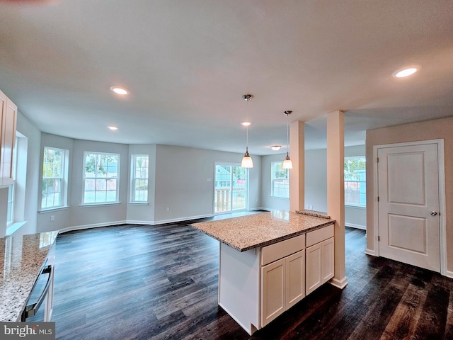 kitchen featuring white cabinets, light stone countertops, hanging light fixtures, and a wealth of natural light