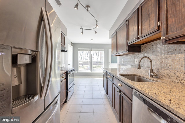 kitchen featuring track lighting, stainless steel appliances, sink, pendant lighting, and light stone counters