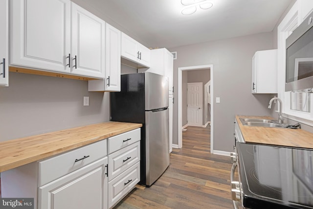 kitchen with appliances with stainless steel finishes, white cabinetry, dark hardwood / wood-style flooring, wooden counters, and sink