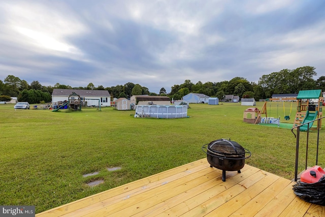 view of yard with a playground, a pool side deck, a storage shed, and a fire pit