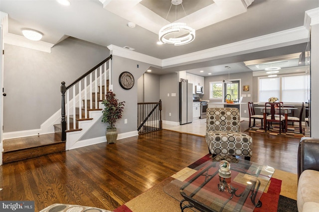 living room featuring ornamental molding, an inviting chandelier, a tray ceiling, and hardwood / wood-style floors