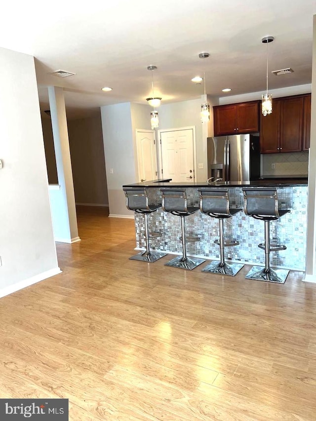 kitchen with hanging light fixtures, stainless steel refrigerator with ice dispenser, light wood-type flooring, and a breakfast bar area