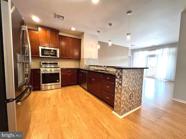 kitchen with sink, kitchen peninsula, decorative light fixtures, light hardwood / wood-style flooring, and appliances with stainless steel finishes