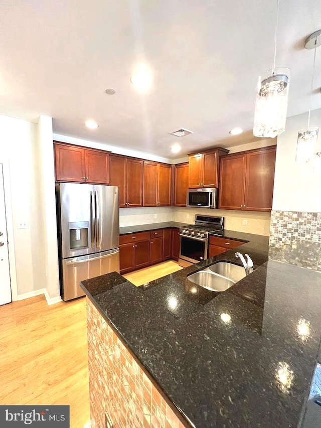 kitchen featuring dark stone counters, light hardwood / wood-style floors, sink, hanging light fixtures, and appliances with stainless steel finishes