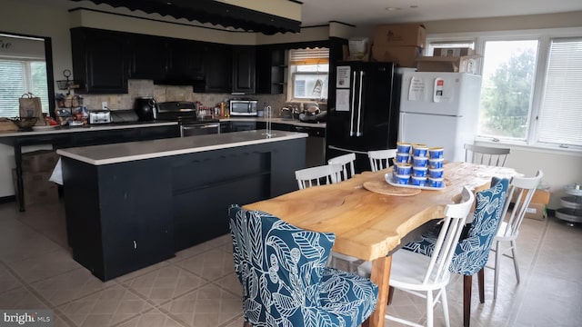 kitchen with light tile patterned flooring, a kitchen island, black appliances, and tasteful backsplash