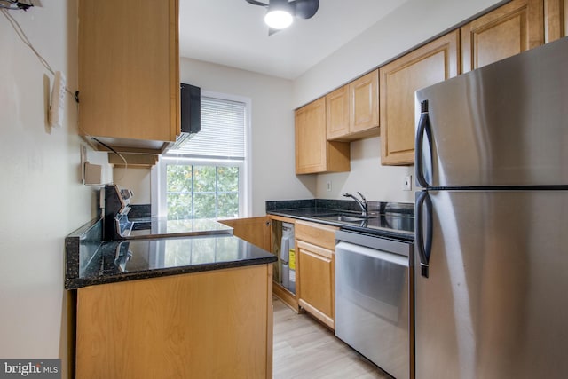 kitchen with sink, dark stone counters, light wood-type flooring, ceiling fan, and stainless steel appliances