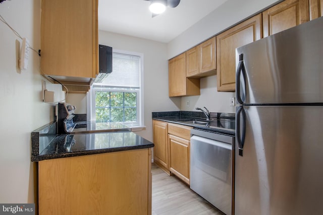 kitchen with stainless steel appliances, light wood-type flooring, a sink, and dark stone counters