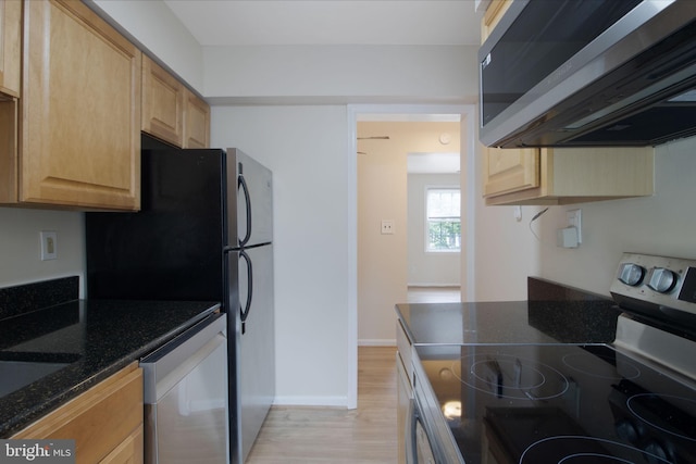 kitchen with stainless steel appliances, dark stone countertops, light brown cabinets, and light hardwood / wood-style floors