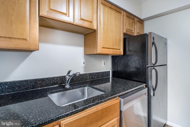 kitchen featuring dark stone counters, stainless steel dishwasher, a sink, and freestanding refrigerator