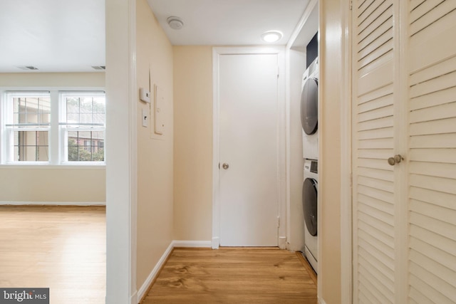 laundry room with baseboards, light wood-type flooring, visible vents, stacked washer / drying machine, and laundry area