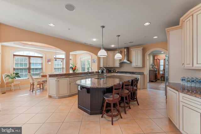 kitchen with wall chimney exhaust hood, arched walkways, cream cabinets, and a kitchen bar