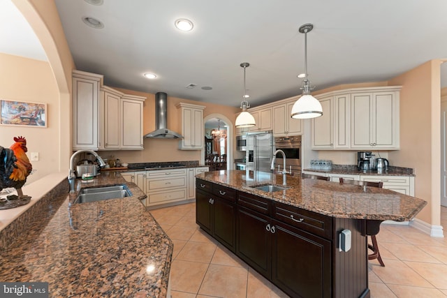 kitchen featuring wall chimney exhaust hood, a breakfast bar, dark stone counters, and sink