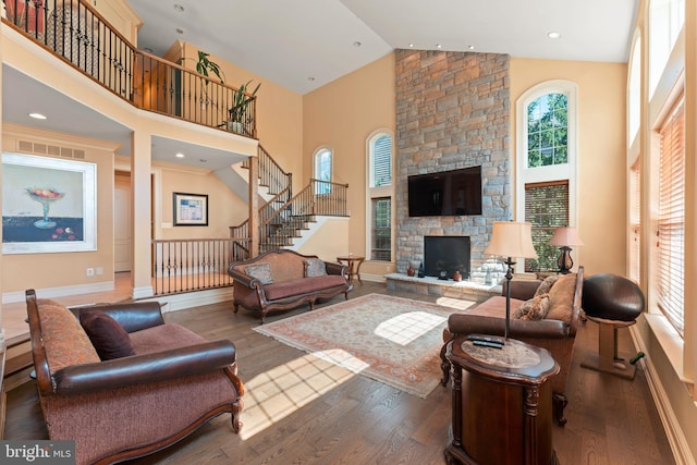 living room with high vaulted ceiling, stairway, wood finished floors, a stone fireplace, and visible vents