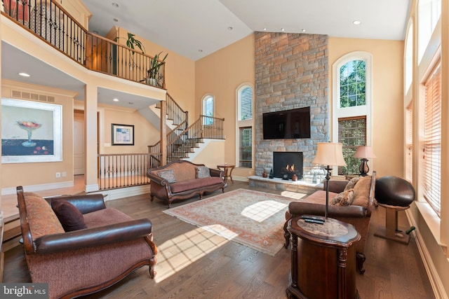 living room featuring stairs, high vaulted ceiling, visible vents, a fireplace, and wood finished floors