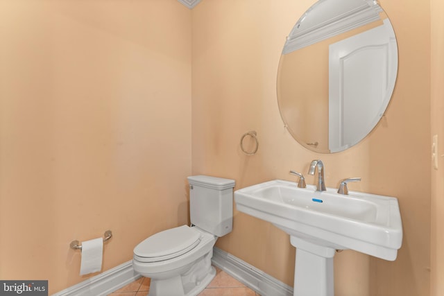 half bath featuring baseboards, toilet, tile patterned flooring, and a sink