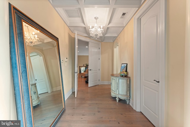 corridor with beamed ceiling, ornamental molding, coffered ceiling, an inviting chandelier, and light wood-type flooring