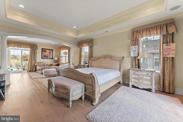 bedroom with decorative columns, crown molding, a raised ceiling, wood finished floors, and arched walkways