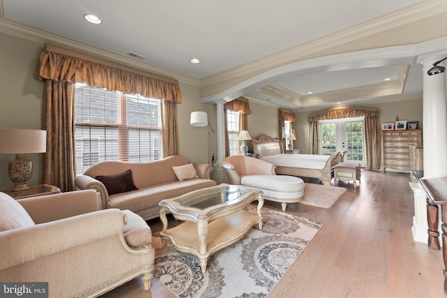 living room with ornate columns, ornamental molding, a raised ceiling, and hardwood / wood-style floors