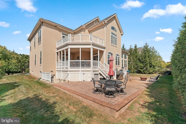back of property with a balcony, a patio, stucco siding, a fire pit, and a yard