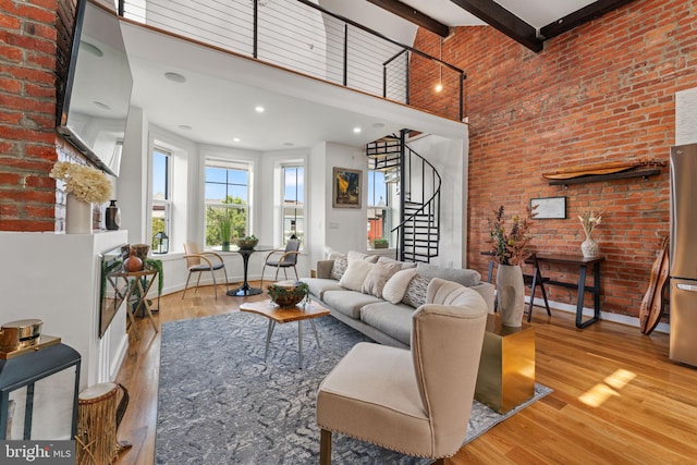 living room with a high ceiling, beamed ceiling, brick wall, and light hardwood / wood-style flooring