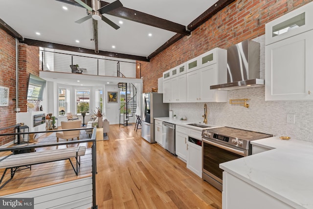 kitchen featuring white cabinets, sink, beam ceiling, wall chimney exhaust hood, and appliances with stainless steel finishes