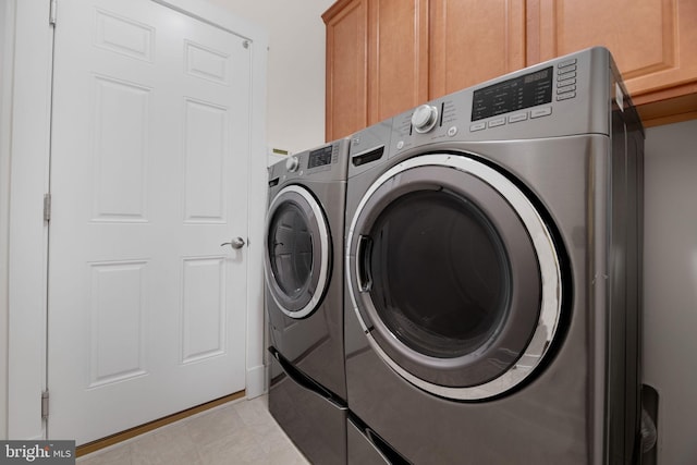 laundry area with washing machine and clothes dryer, light tile patterned floors, and cabinets