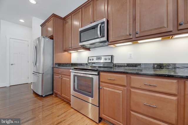 kitchen with appliances with stainless steel finishes, dark stone counters, and light hardwood / wood-style floors