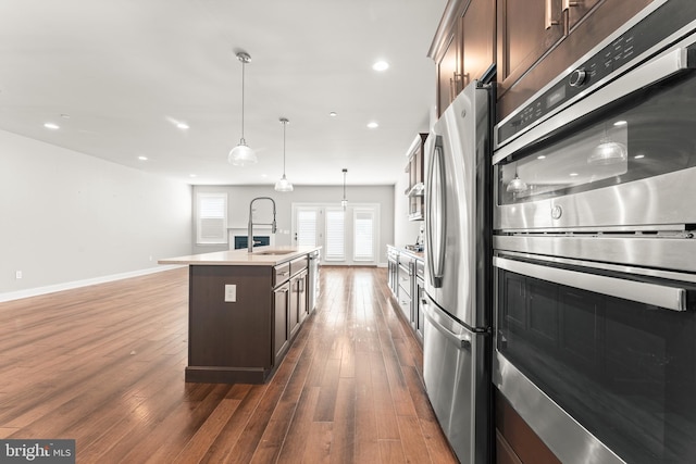 kitchen featuring dark wood-type flooring, sink, an island with sink, stainless steel appliances, and dark brown cabinetry