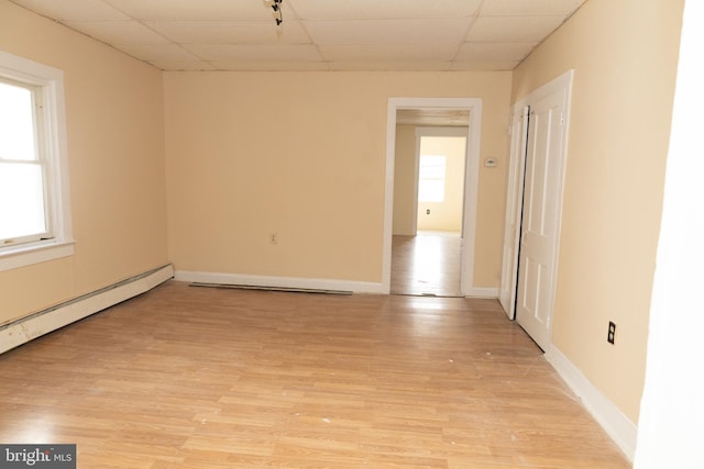 empty room with baseboard heating, a drop ceiling, and light wood-type flooring