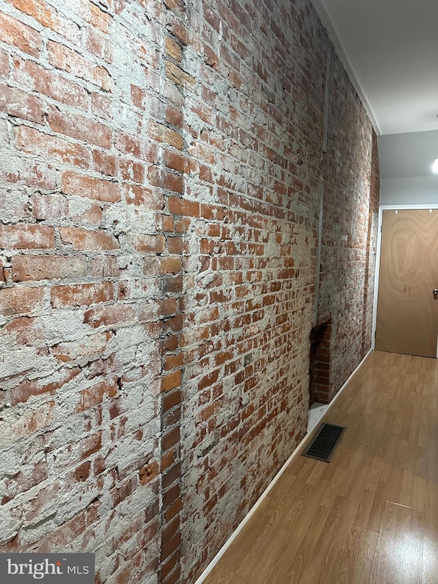 hallway with brick wall and hardwood / wood-style flooring