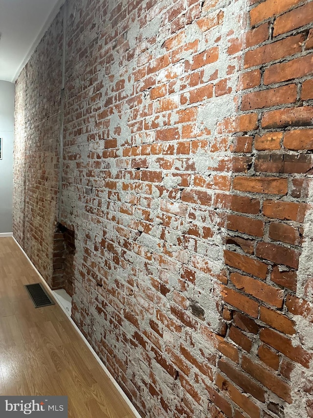 hallway with brick wall and hardwood / wood-style floors