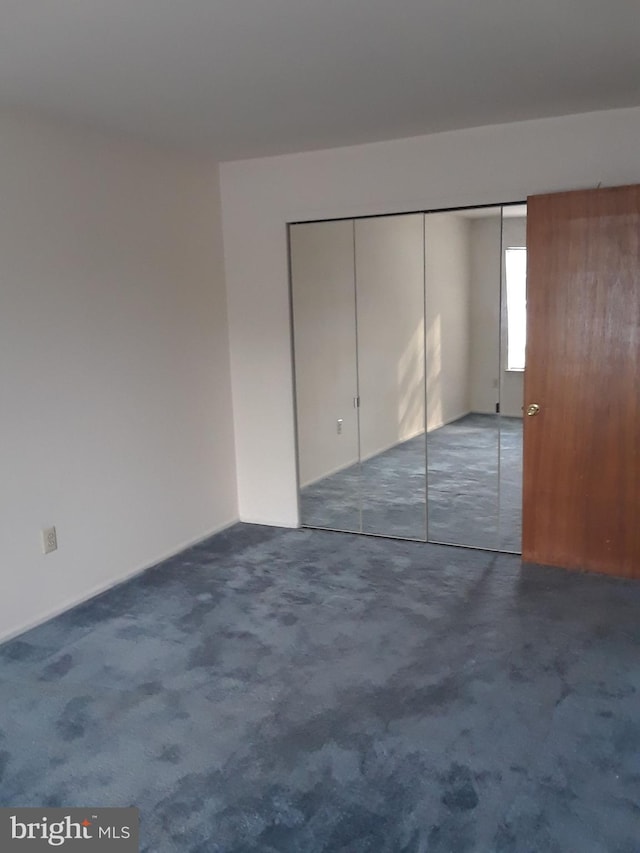 unfurnished bedroom featuring dark colored carpet and a closet