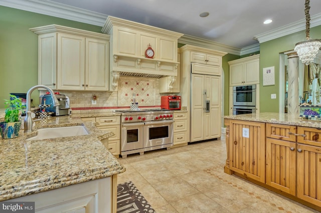 kitchen featuring sink, hanging light fixtures, high quality appliances, light stone counters, and cream cabinetry