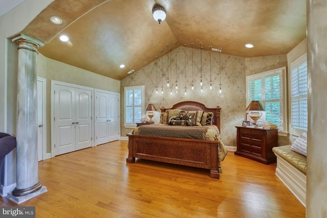 bedroom with decorative columns, vaulted ceiling, two closets, and light wood-type flooring