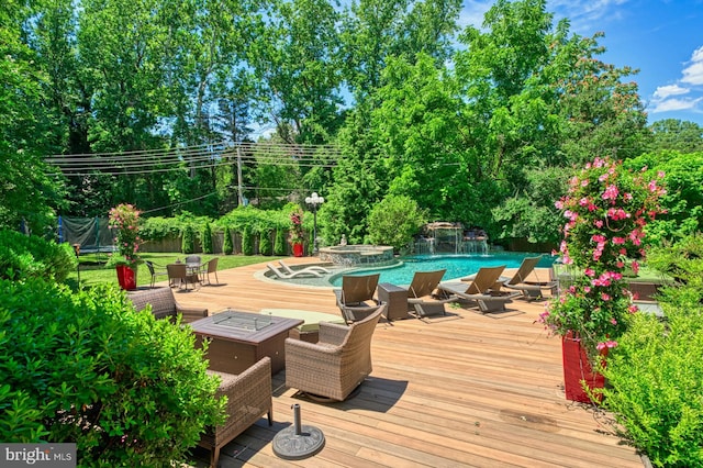 view of swimming pool with an in ground hot tub, pool water feature, a deck, and a trampoline