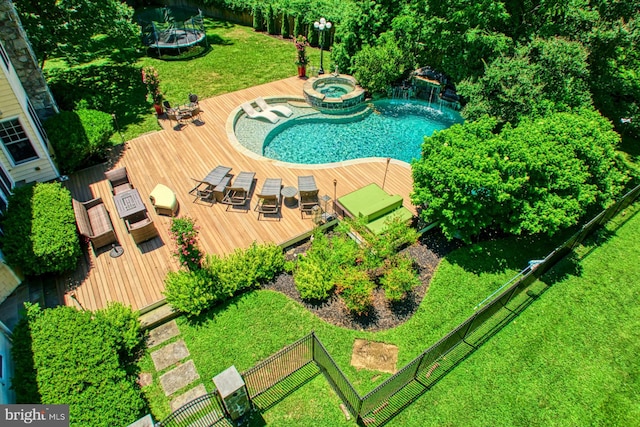 view of swimming pool featuring a wooden deck, an in ground hot tub, a trampoline, and a lawn