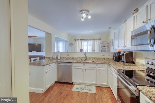 kitchen with white cabinets, kitchen peninsula, stainless steel appliances, light wood-type flooring, and sink