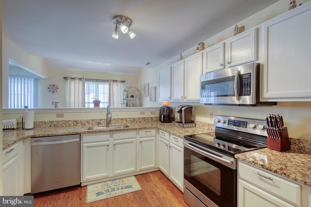 kitchen with sink, white cabinetry, stainless steel appliances, light stone countertops, and light hardwood / wood-style floors