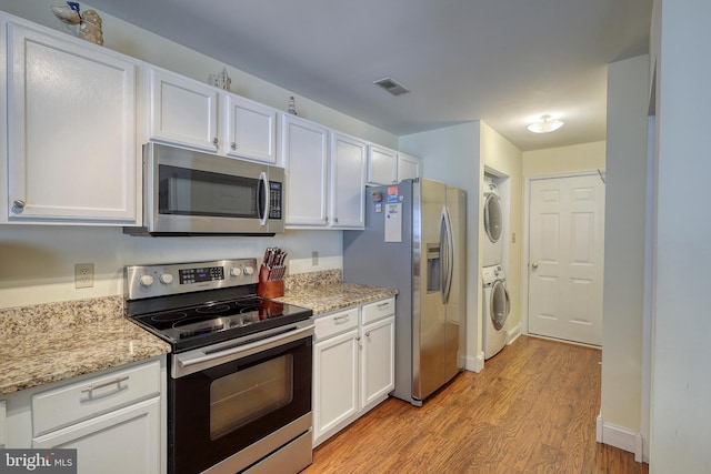 kitchen featuring light stone counters, white cabinets, stacked washing maching and dryer, light hardwood / wood-style flooring, and appliances with stainless steel finishes