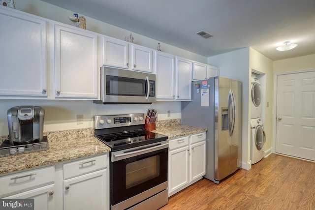 kitchen featuring light hardwood / wood-style floors, stacked washing maching and dryer, white cabinets, light stone countertops, and stainless steel appliances