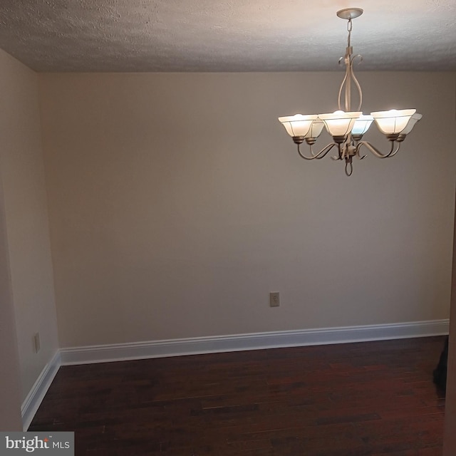 empty room with a notable chandelier, a textured ceiling, and dark wood-type flooring