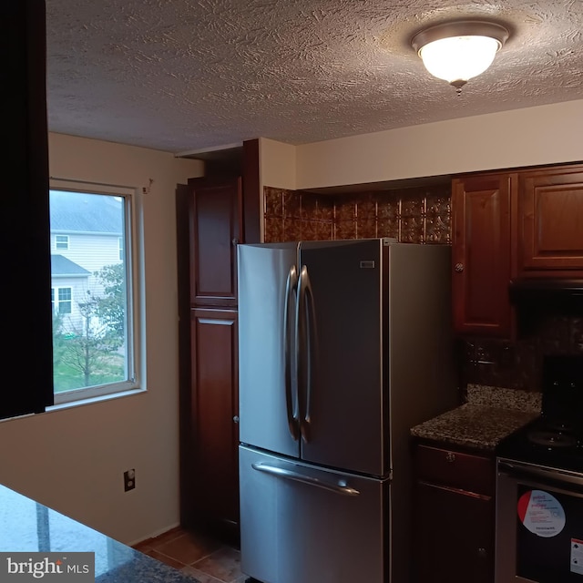 kitchen with black / electric stove, stainless steel refrigerator, dark stone counters, and a textured ceiling