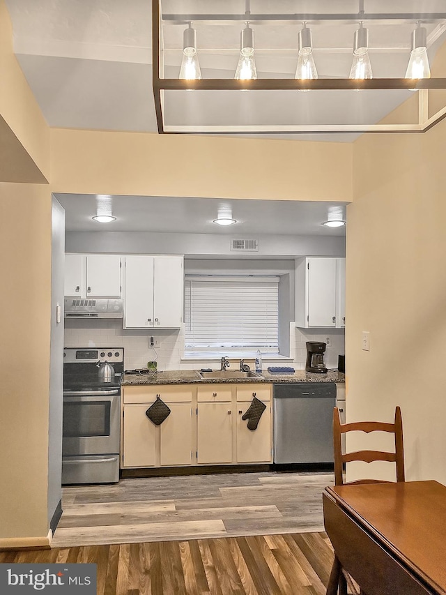 kitchen featuring appliances with stainless steel finishes, decorative light fixtures, light hardwood / wood-style floors, and white cabinetry